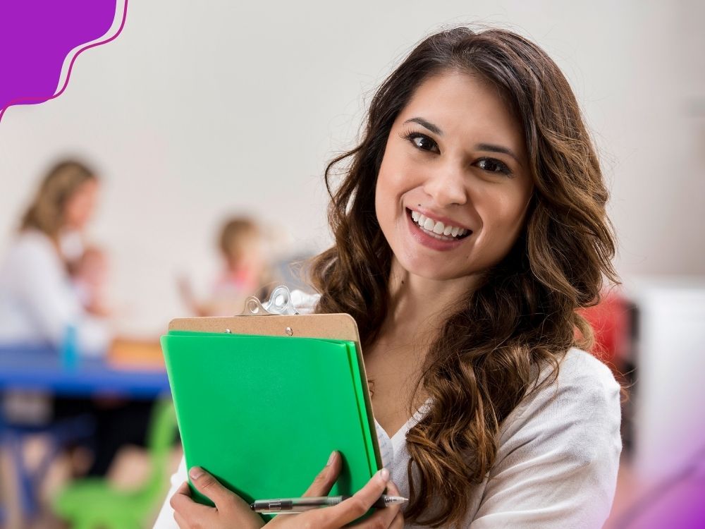 Professora segurando uma prancheta e pastinhas, e uma caneta em uma das mãos, como se estivesse anotando as observações em sala de aula.