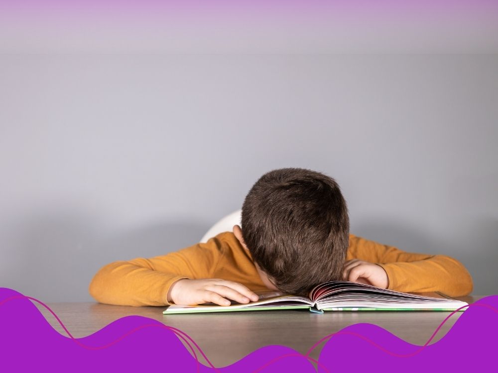 Criança deitada sobre um caderno, demonstrando desmotivação e frustração devido às dificuldades no aprendizado da leitura e escrita.
