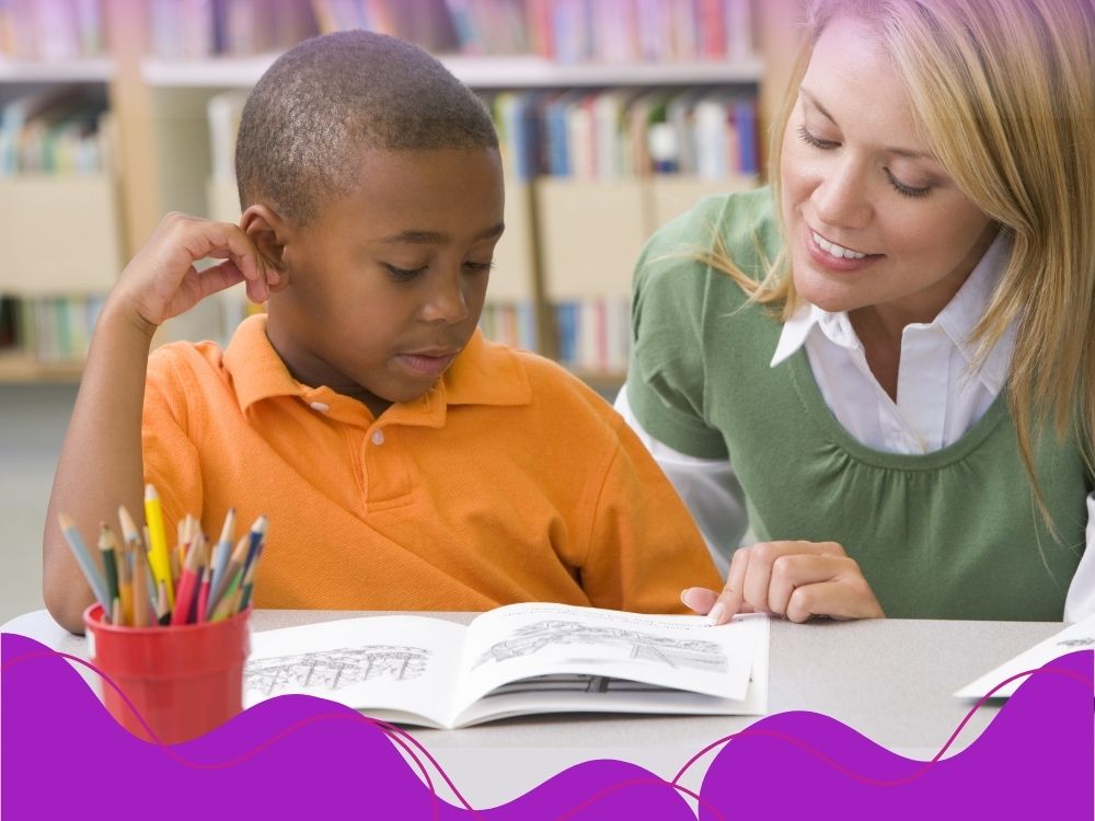 Professora auxiliando um aluno a ler, para ilustrar a intervenção pedagógica para alfabetização relacionada às habilidades de leitura.