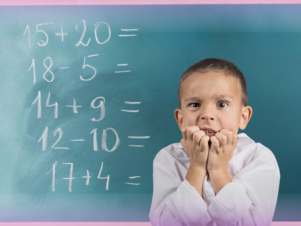 Aluno roendo as unhas, ansioso e ao fundo uma lousa com expressões matemáticas escritas com giz. A imagem ilustra o que é ansiedade matemática e os sintomas.