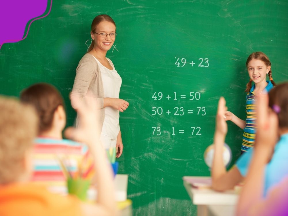 Aluna, próxima ao quadro/lousa, explicando para os colegas a resolução de um cálculo por arredondamento para resolver 49+23 (49+1=50;50+23=73; 73-1=72). A imagem ilustra a importância das conversas numéricas para desenvolver o senso numérico.